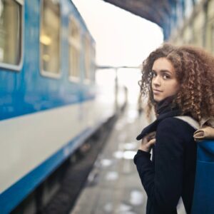 Woman in black coat standing beside blue and white train
